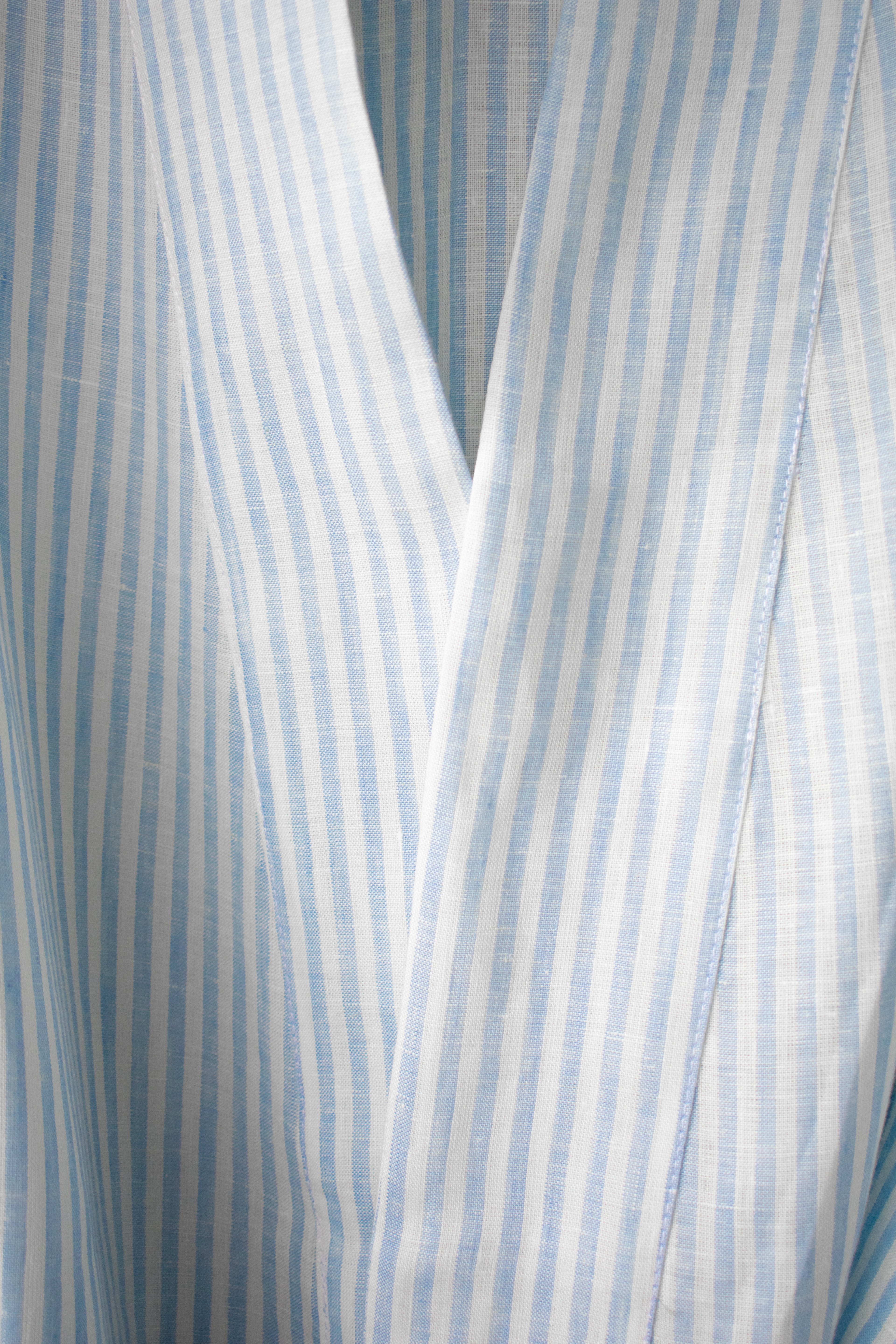 Upper neckline of a tied wide falling kimono in light blue and white stripes. The coat is wide and made of summery linen.